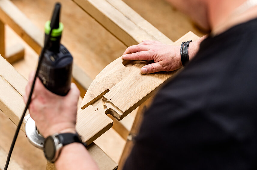 Stolarz podczas ręcznego frezowania elementu z litego drewna dębowego w trakcie produkcji mebli na wymiar